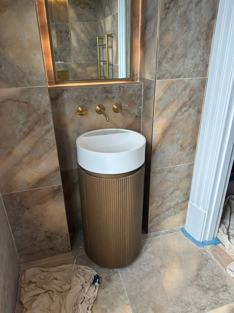 Round basin on a fluted pedestal with wall-mounted brass taps and lit mirror