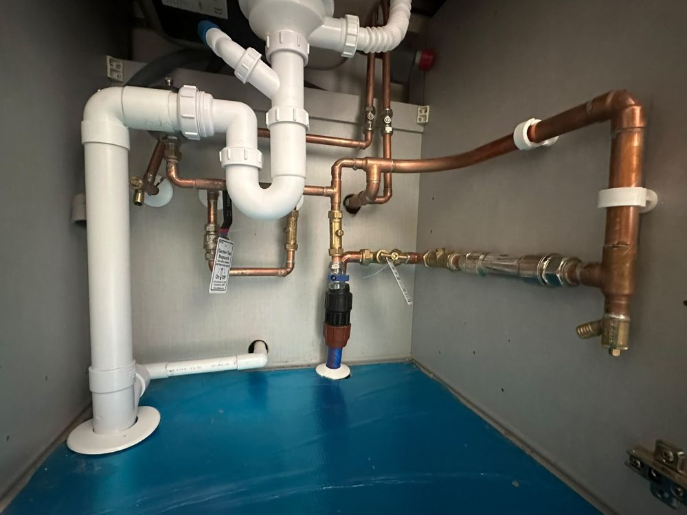 Under-sink plumbing with copper pipework, isolation valves and a labelled stopcock